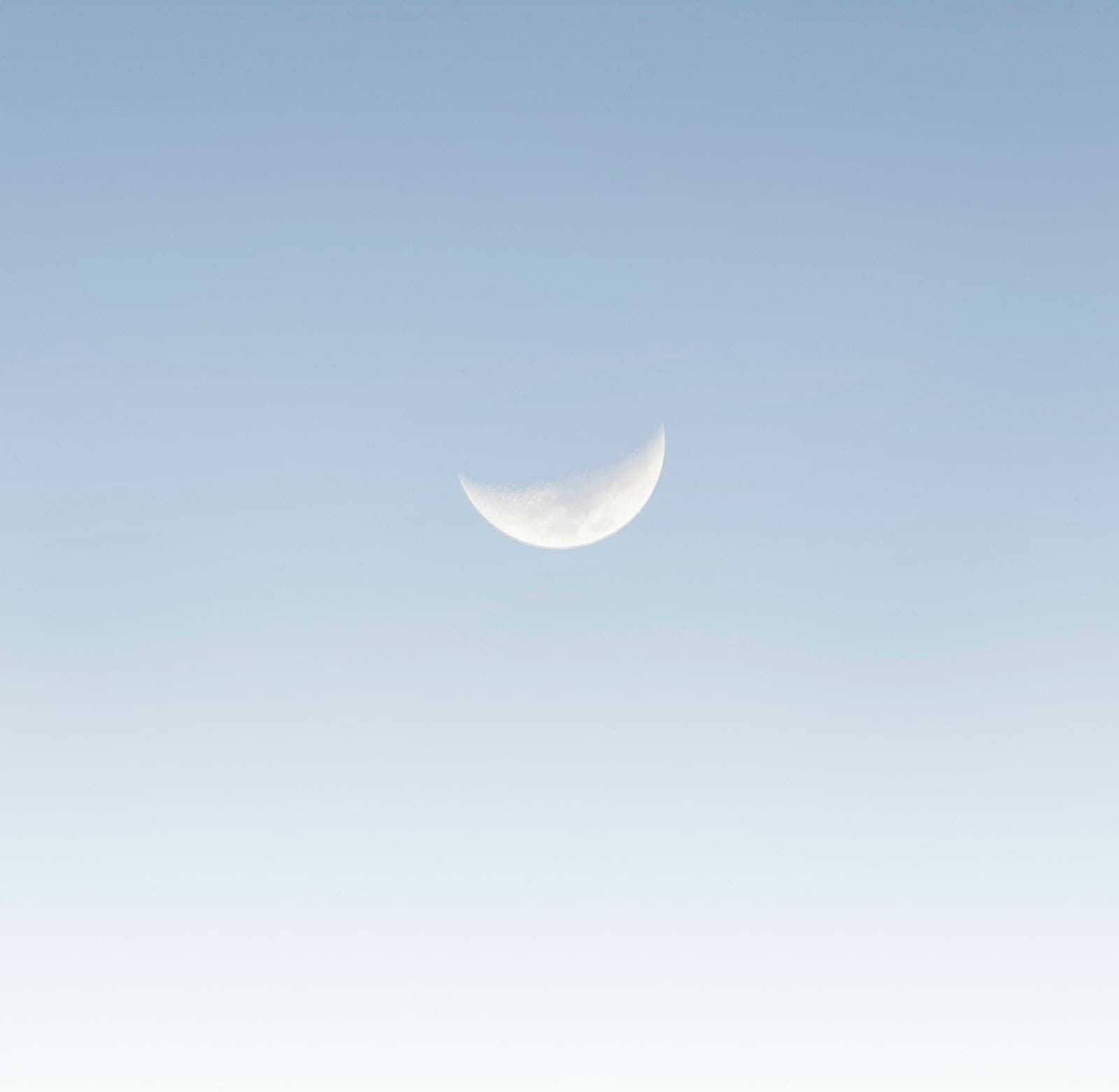A waxing crescent moon high in a clear, pale blue sky.